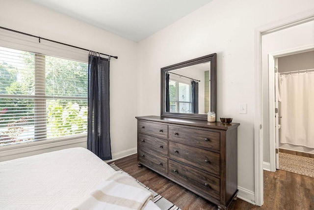 bedroom with dark wood finished floors, a walk in closet, and baseboards