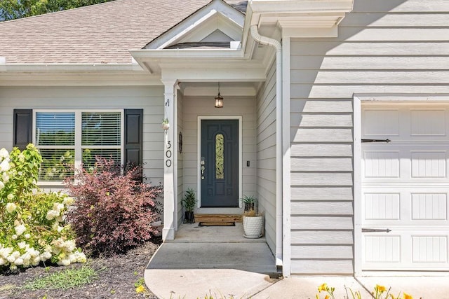 view of exterior entry with an attached garage and roof with shingles