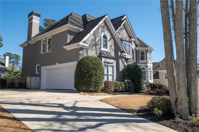 view of front facade featuring driveway, a chimney, an attached garage, and stucco siding