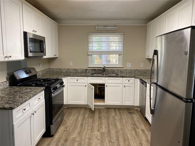 kitchen featuring sink, dark stone countertops, ornamental molding, appliances with stainless steel finishes, and white cabinetry