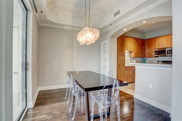 dining room with dark wood-type flooring, crown molding, a raised ceiling, and an inviting chandelier