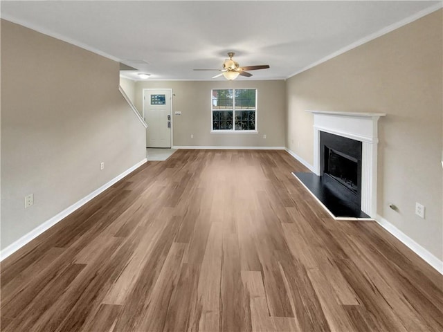 unfurnished living room featuring wood finished floors, a fireplace with raised hearth, baseboards, and ornamental molding