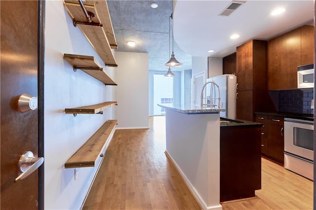 kitchen featuring pendant lighting, white appliances, a center island with sink, decorative backsplash, and light wood-type flooring