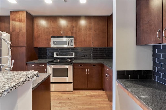 kitchen with stainless steel appliances, dark stone countertops, backsplash, and light hardwood / wood-style floors