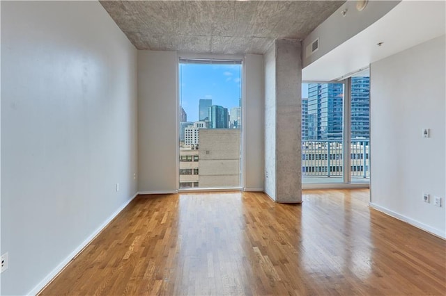 unfurnished room featuring plenty of natural light, a wall of windows, and light hardwood / wood-style floors