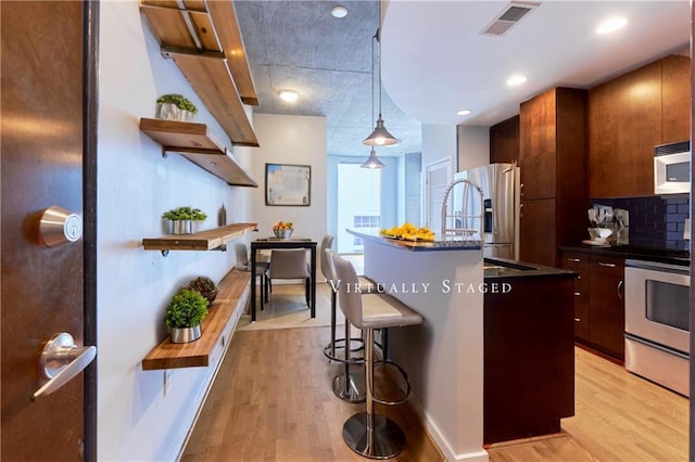 kitchen with decorative light fixtures, light wood-type flooring, stainless steel appliances, and a center island with sink