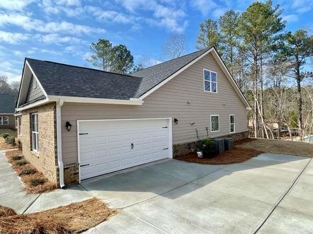 view of property exterior featuring a shingled roof, brick siding, driveway, and a garage