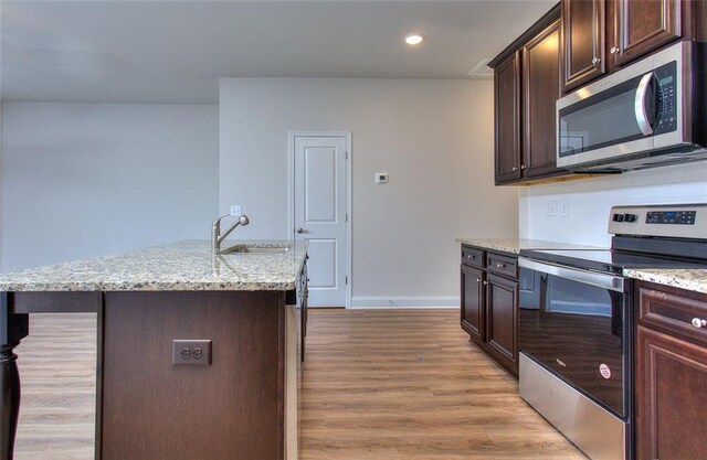 kitchen with a center island with sink, backsplash, light hardwood / wood-style floors, stainless steel appliances, and sink