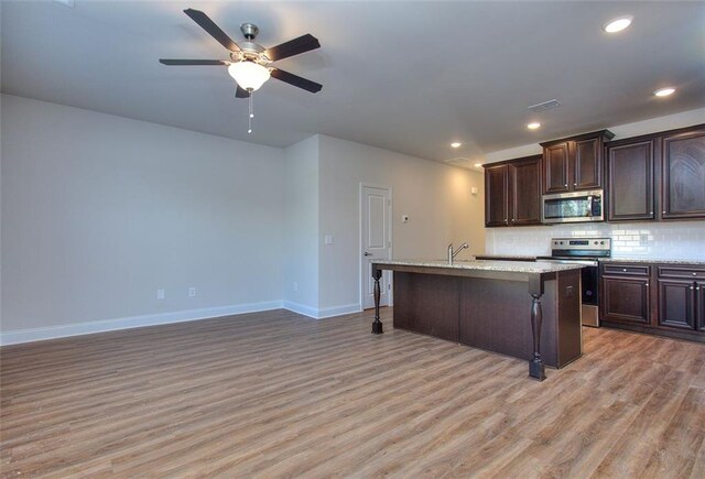 kitchen featuring light wood-type flooring, appliances with stainless steel finishes, a center island with sink, and a breakfast bar