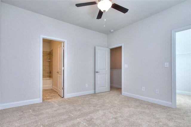 unfurnished bedroom featuring ceiling fan, connected bathroom, a spacious closet, and light carpet