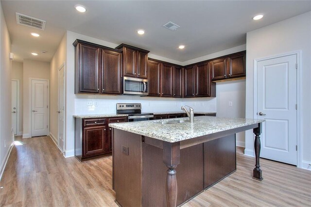 kitchen with light stone countertops, a center island with sink, appliances with stainless steel finishes, light hardwood / wood-style floors, and sink