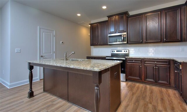 kitchen with sink, hardwood / wood-style floors, appliances with stainless steel finishes, and a kitchen island with sink