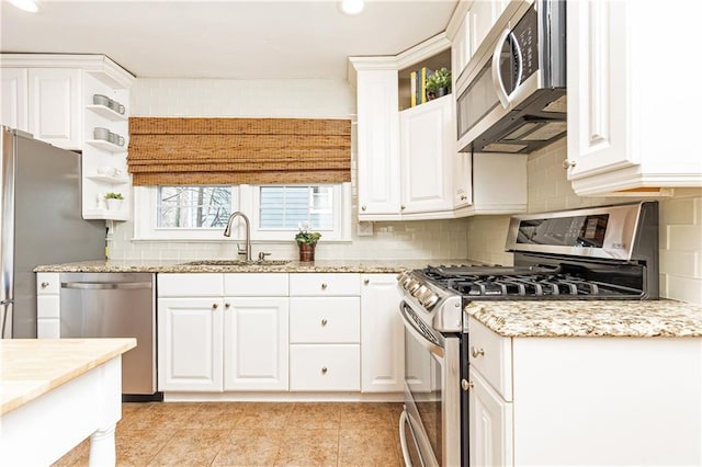 kitchen featuring appliances with stainless steel finishes, white cabinetry, sink, backsplash, and light stone countertops