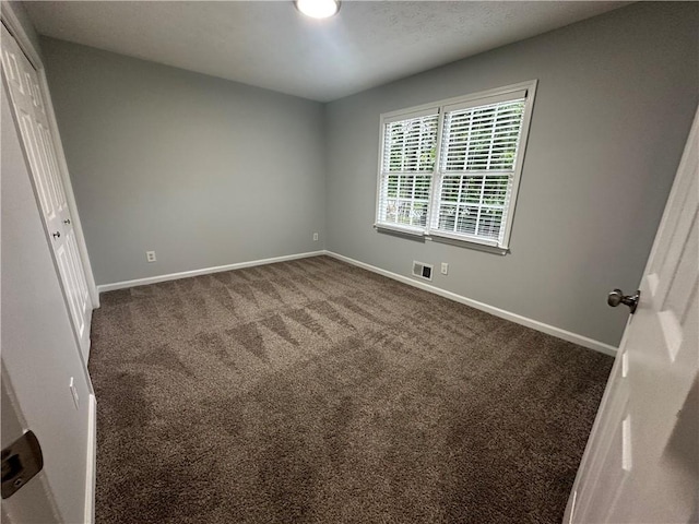 unfurnished bedroom featuring baseboards, dark carpet, and a closet