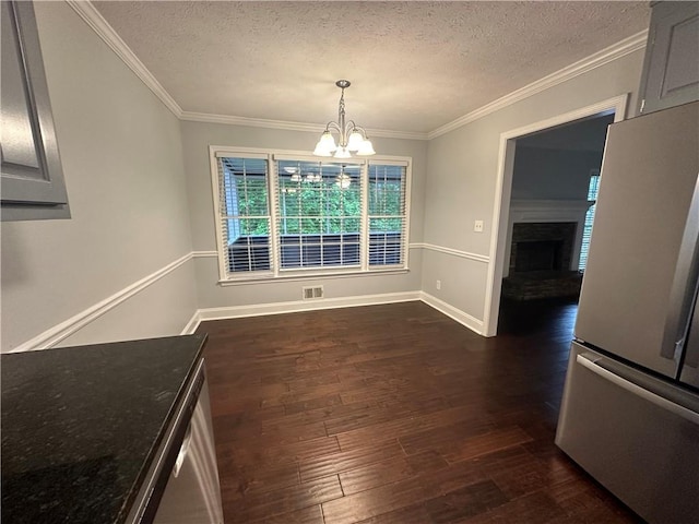 unfurnished dining area with dark wood finished floors, a chandelier, a textured ceiling, ornamental molding, and a fireplace with raised hearth