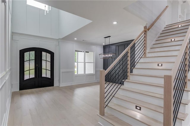 foyer with light wood-type flooring, french doors, arched walkways, a decorative wall, and stairs