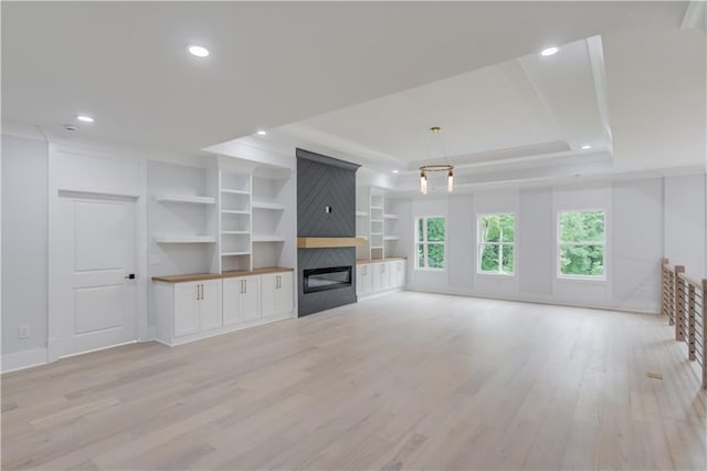 unfurnished living room featuring light wood-type flooring, a glass covered fireplace, recessed lighting, baseboards, and a raised ceiling