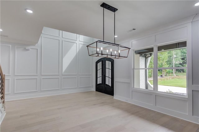 unfurnished dining area with visible vents, recessed lighting, light wood-style flooring, a notable chandelier, and a decorative wall