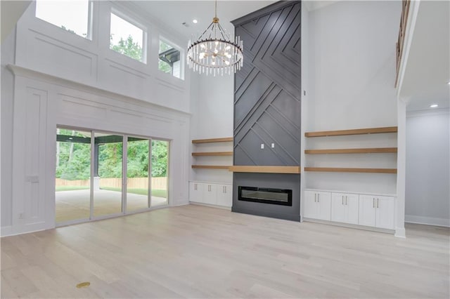 unfurnished living room with light wood finished floors, a large fireplace, baseboards, an inviting chandelier, and a towering ceiling