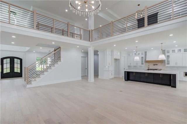 unfurnished living room with stairway, an inviting chandelier, light wood-type flooring, and a towering ceiling