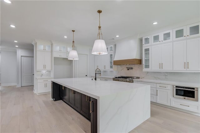 kitchen featuring premium range hood, light wood-style flooring, a large island, white cabinetry, and a sink