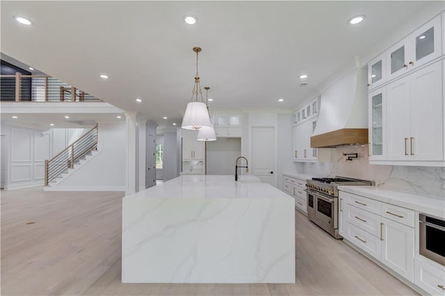 kitchen with light wood finished floors, custom exhaust hood, range with two ovens, decorative backsplash, and white cabinets