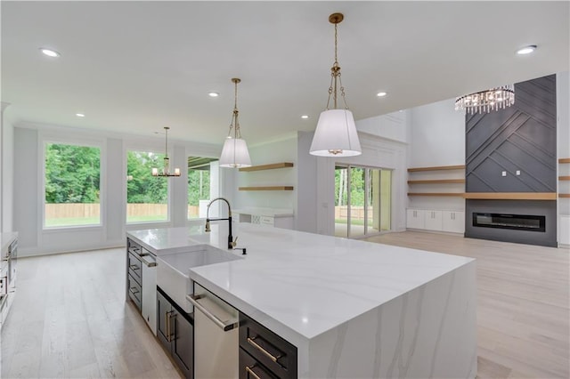 kitchen featuring a large fireplace, a center island with sink, dishwasher, light wood-type flooring, and a sink