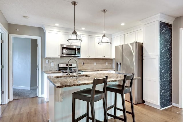 kitchen featuring white cabinetry, stainless steel appliances, dark stone countertops, a kitchen island with sink, and light wood-type flooring