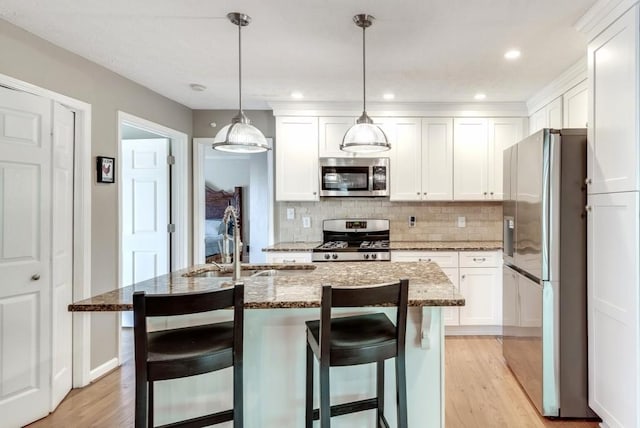 kitchen featuring hanging light fixtures, an island with sink, light hardwood / wood-style floors, white cabinetry, and stainless steel appliances