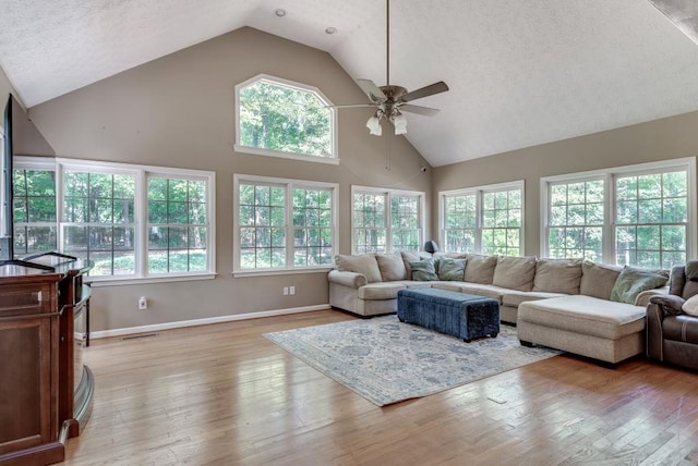 living room with ceiling fan, light hardwood / wood-style flooring, high vaulted ceiling, and a healthy amount of sunlight