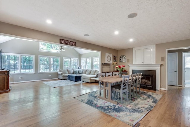 dining area with lofted ceiling, ceiling fan, light wood-type flooring, a textured ceiling, and a fireplace