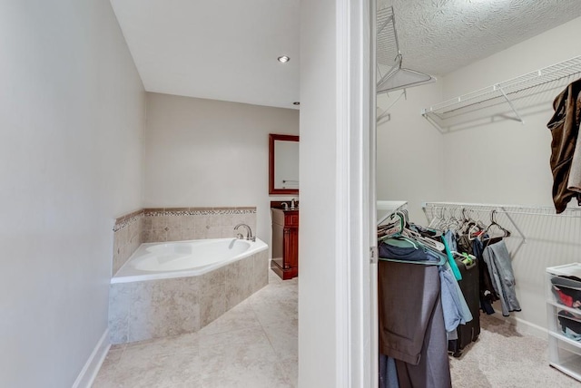 bathroom with tile patterned flooring, vanity, a relaxing tiled tub, and a textured ceiling