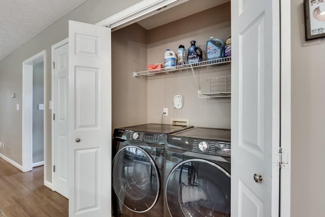 clothes washing area with washer and dryer, a textured ceiling, and hardwood / wood-style flooring