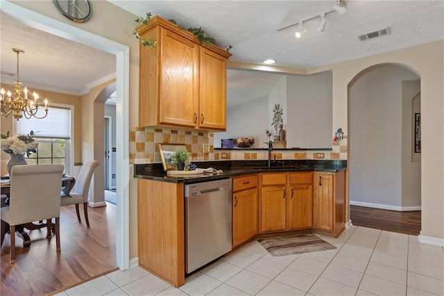kitchen featuring an inviting chandelier, stainless steel dishwasher, a sink, arched walkways, and a textured ceiling
