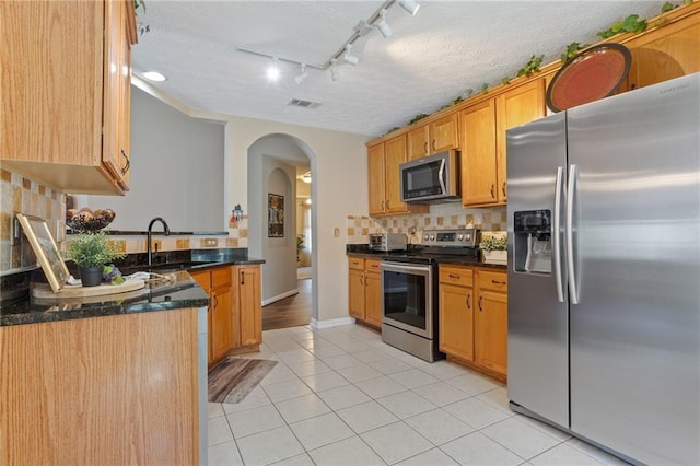 kitchen featuring a sink, stainless steel appliances, rail lighting, visible vents, and arched walkways