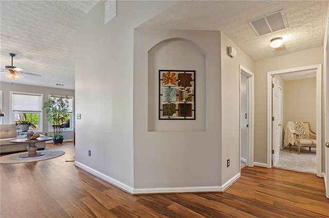 hall with baseboards, wood finished floors, a textured ceiling, and visible vents