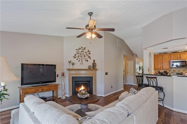 living room featuring ceiling fan, vaulted ceiling, visible vents, a lit fireplace, and dark wood-style flooring