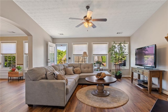 living area featuring wood finished floors, a ceiling fan, visible vents, and arched walkways