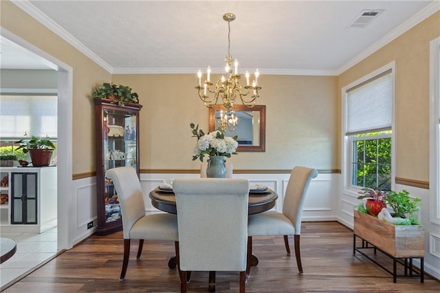 dining area featuring wainscoting, visible vents, a chandelier, wood finished floors, and crown molding