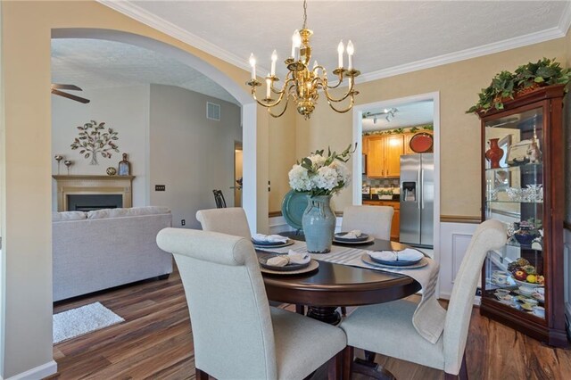 dining area with visible vents, arched walkways, ornamental molding, dark wood-type flooring, and ceiling fan with notable chandelier