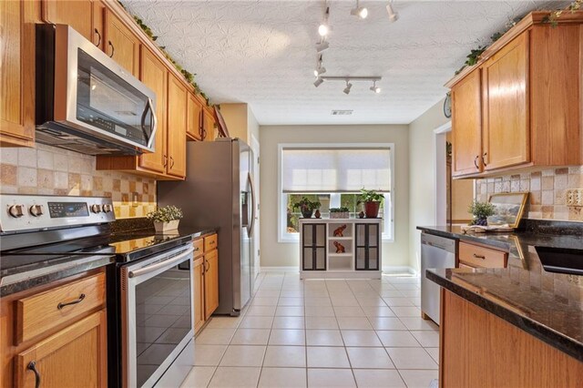 kitchen with decorative backsplash, dark stone counters, light tile patterned floors, stainless steel appliances, and baseboards