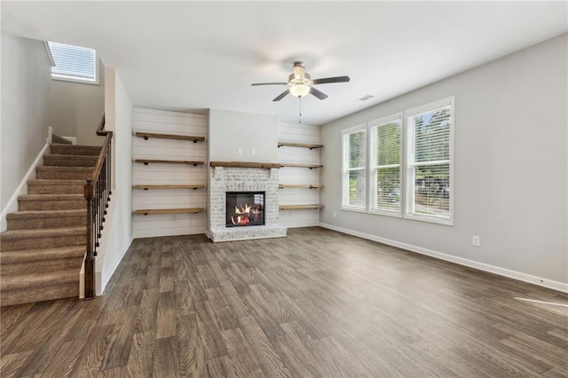 unfurnished living room with a skylight, ceiling fan, dark hardwood / wood-style floors, and a brick fireplace