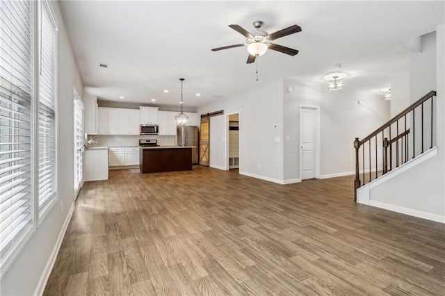 kitchen featuring stainless steel appliances, a barn door, a center island, white cabinetry, and hanging light fixtures