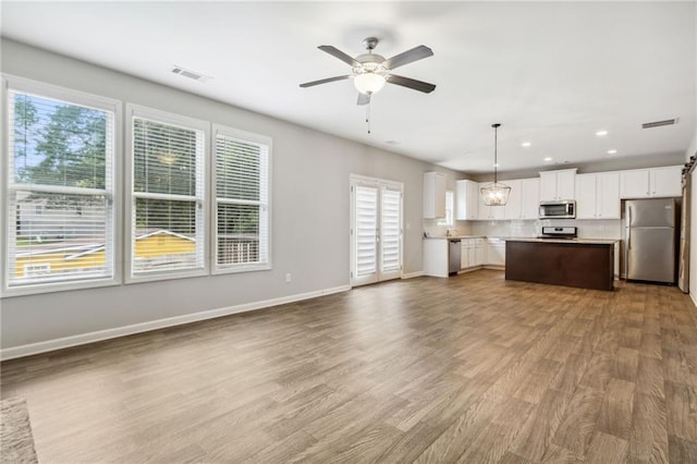 kitchen featuring stainless steel appliances, a kitchen island, wood-type flooring, white cabinetry, and hanging light fixtures