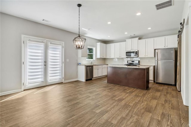 kitchen with dark wood-type flooring, hanging light fixtures, a kitchen island, white cabinets, and appliances with stainless steel finishes