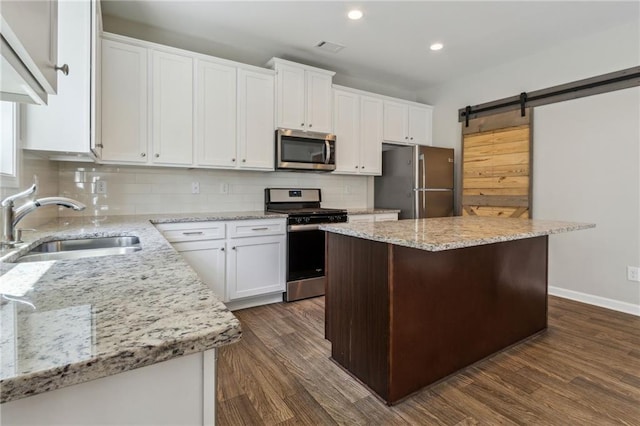 kitchen featuring white cabinetry, sink, stainless steel appliances, a barn door, and a kitchen island