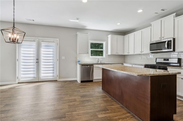 kitchen with hanging light fixtures, a kitchen island, dark hardwood / wood-style floors, white cabinets, and appliances with stainless steel finishes