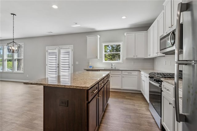 kitchen featuring light stone counters, dark brown cabinetry, stainless steel appliances, a center island, and hanging light fixtures