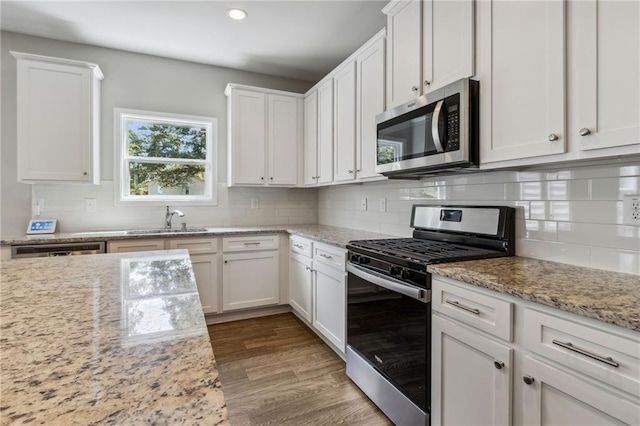 kitchen featuring white cabinets, light stone counters, stainless steel appliances, and hardwood / wood-style floors