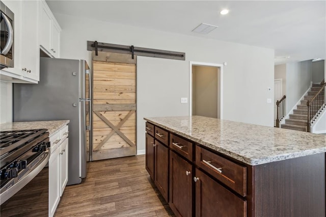 kitchen with dark brown cabinetry, stainless steel appliances, dark wood-type flooring, a barn door, and white cabinets